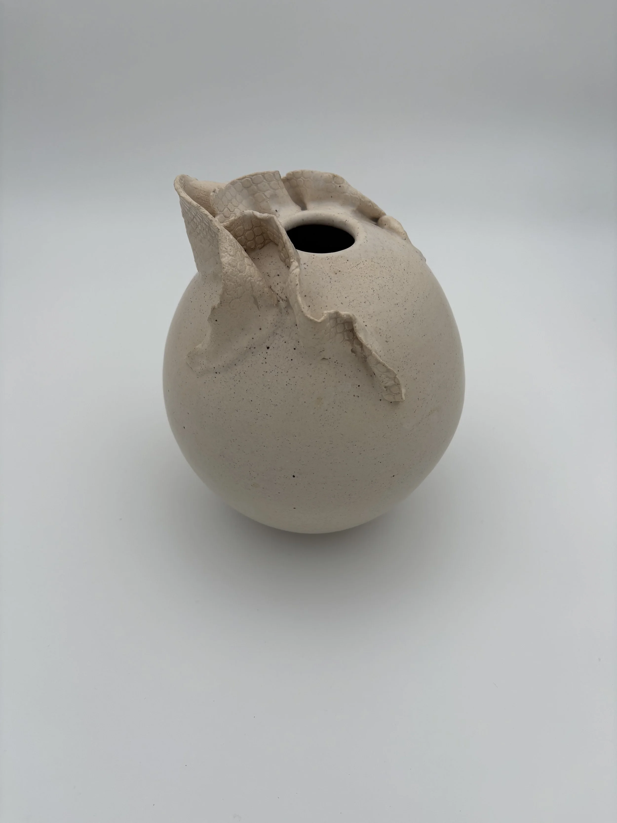 Cream-colored ceramic vase with a damaged top, showing torn and uneven edges.
