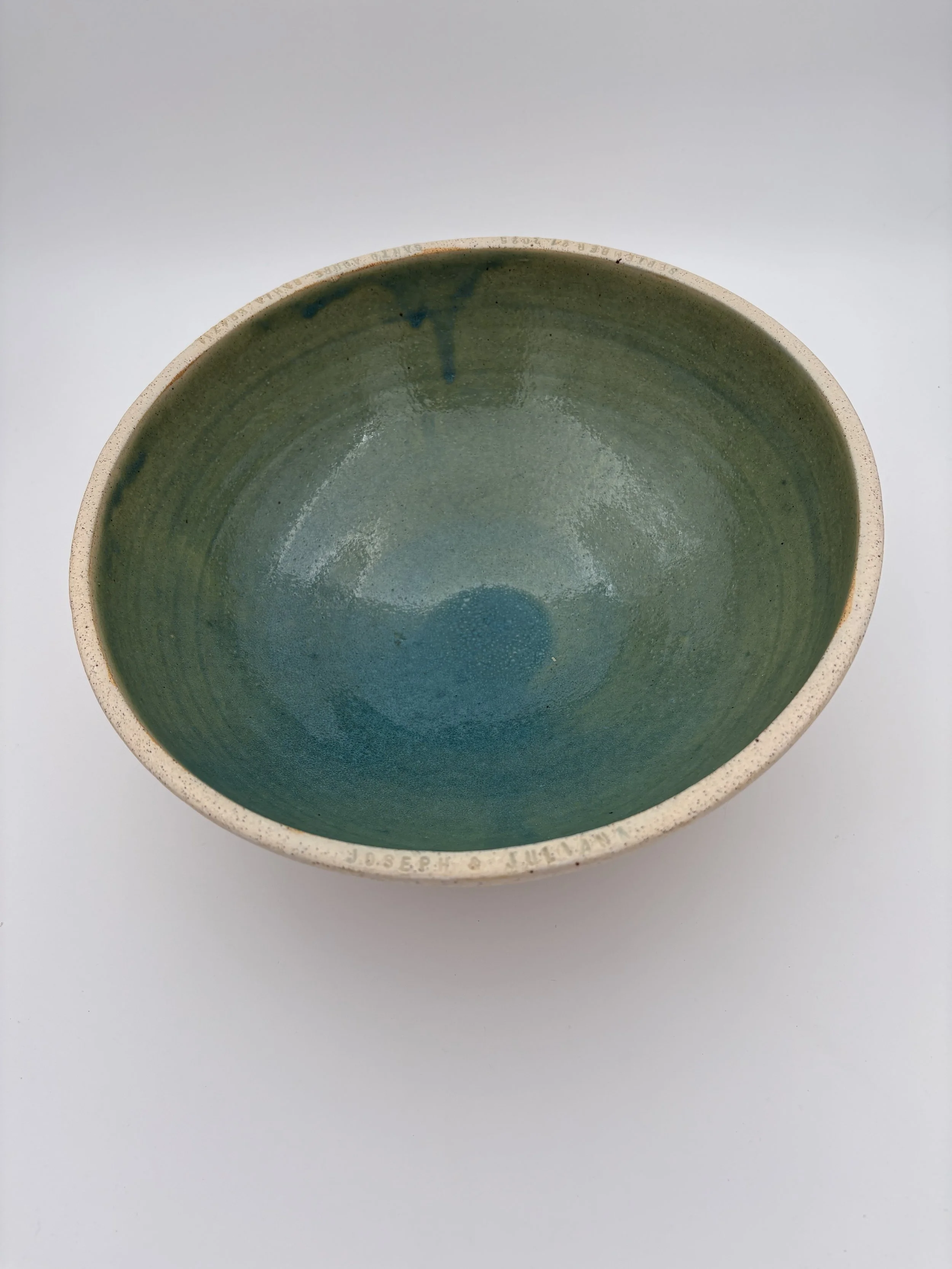 A ceramic bowl with a green glazed interior and an unglazed, speckled beige exterior, placed on a white surface.