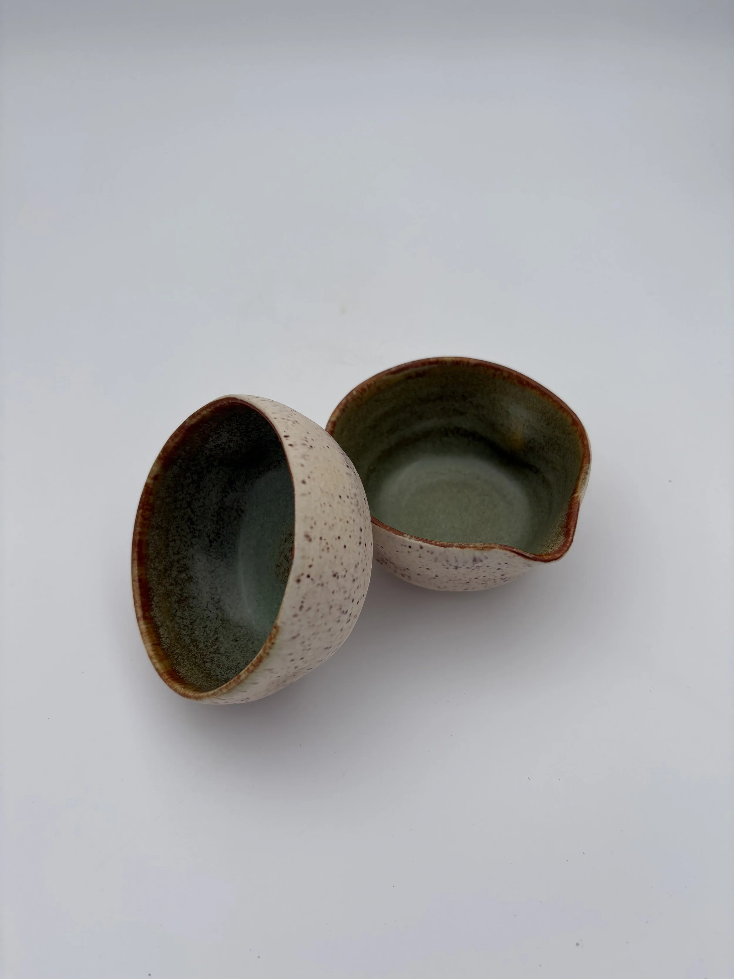 Two small ceramic cups with speckled exterior and greenish interior, placed on a white surface.