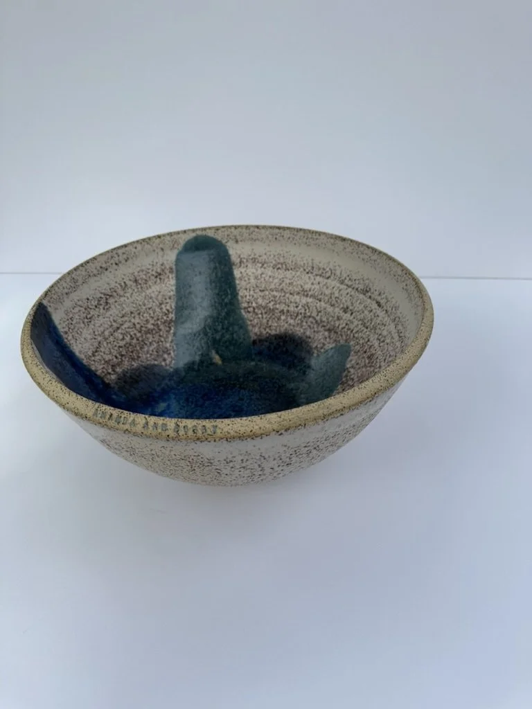 A ceramic bowl with a speckled beige exterior and a dark blue interior, featuring a small sculpture of a cat inside.