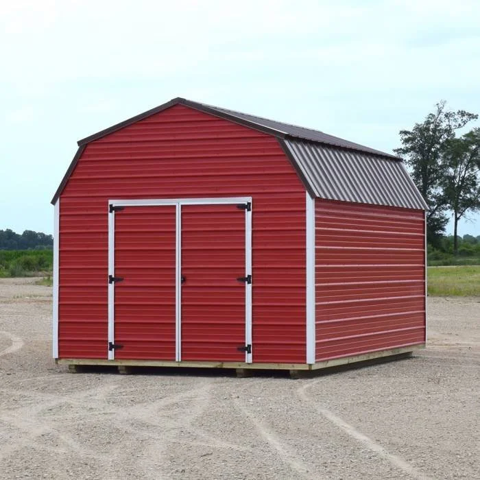 A red barn-style shed with white trim and a black metal roof, situated on a dirt lot outdoors with trees in the background.