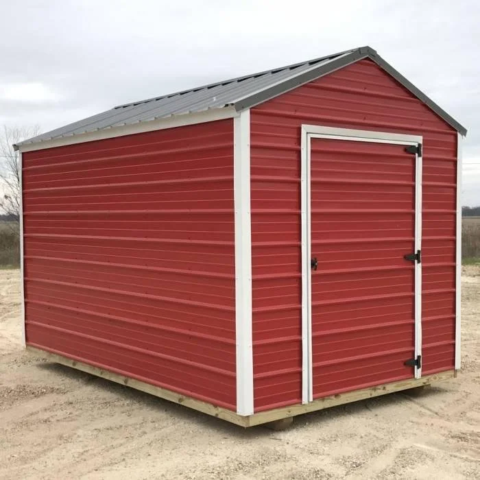 Red metal storage shed with white trim and a gray metal roof on a dirt lot.
