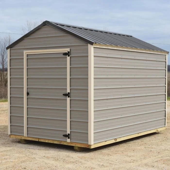 A small beige metal storage shed with a gable roof and double door, placed on wooden pallets on a dirt ground.
