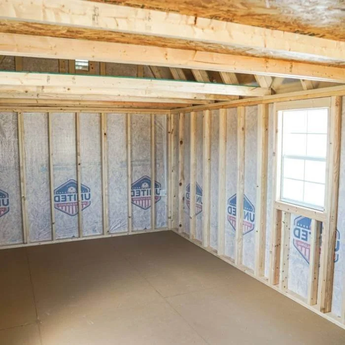 Interior of a portable building with framing, insulation, an unfinished roof, and a window.