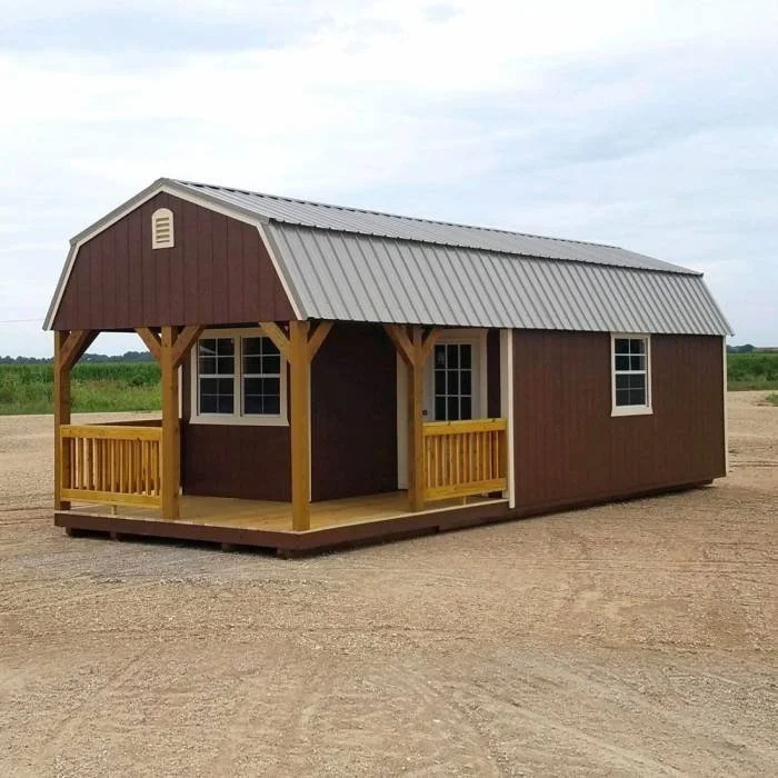 Large brown cabin with a porch and metal roof, situated on a dirt lot.