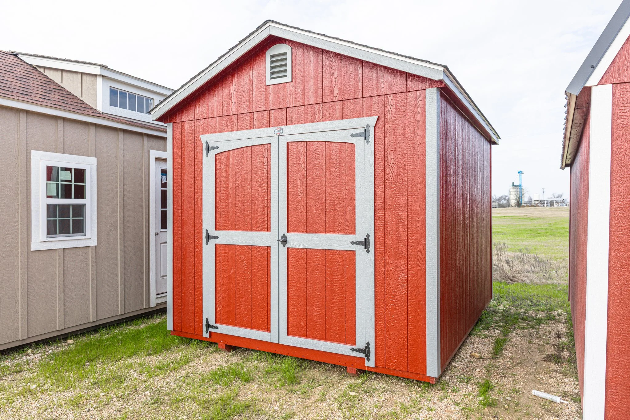 A red wooden shed with white trim and black hinges, situated outside on a grassy area.
