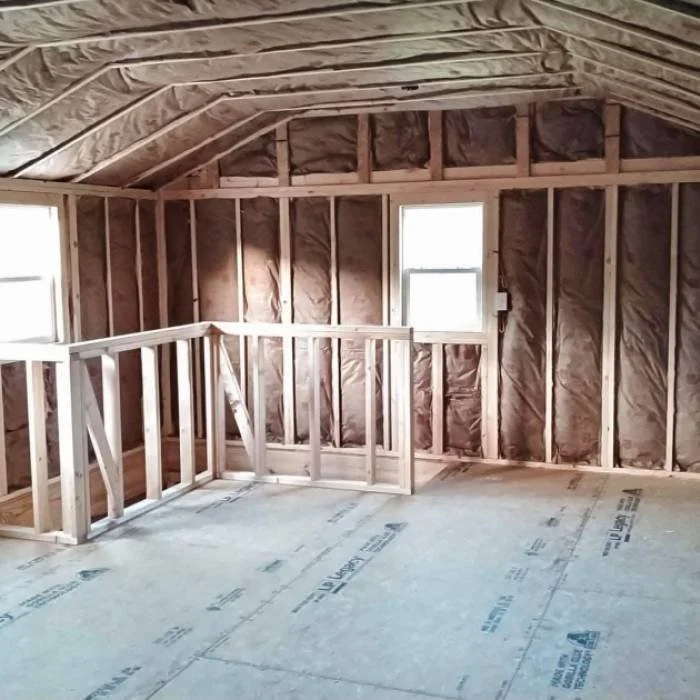 Interior of an unfinished room with exposed wooden framing, insulation, and two windows.