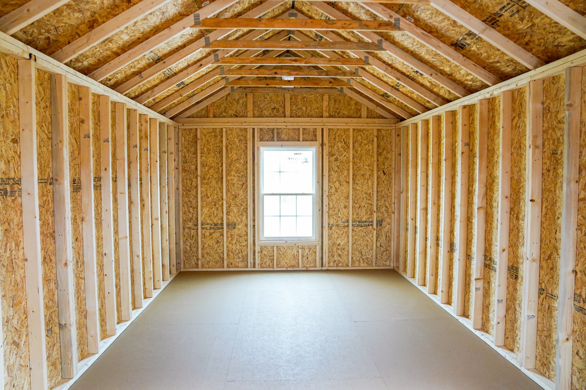 Interior view of an unfinished portable building with exposed wooden framing, insulation panels, and a single window on the far wall.