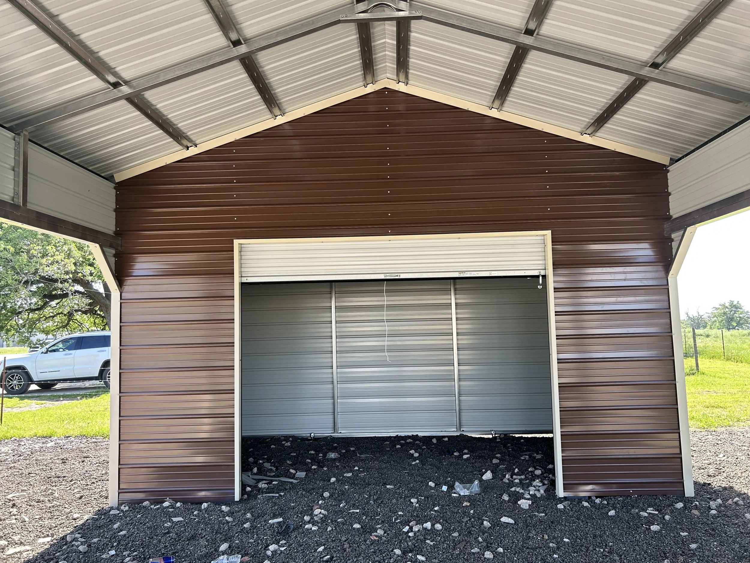 View inside a newly constructed metal storage shed with brown and white walls and a concrete floor with rocks and trash.