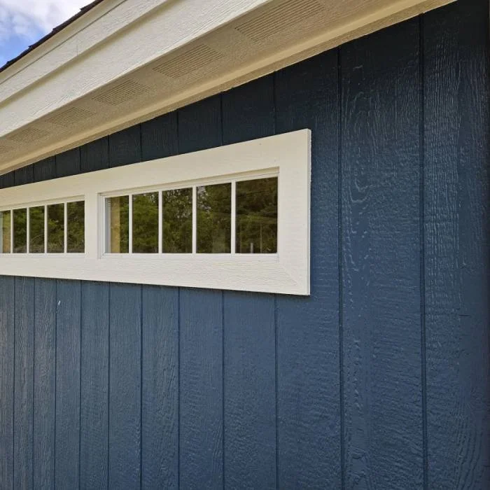 Close-up of a blue exterior wall with vertical wooden siding, showing a long horizontal narrow window with white trim.
