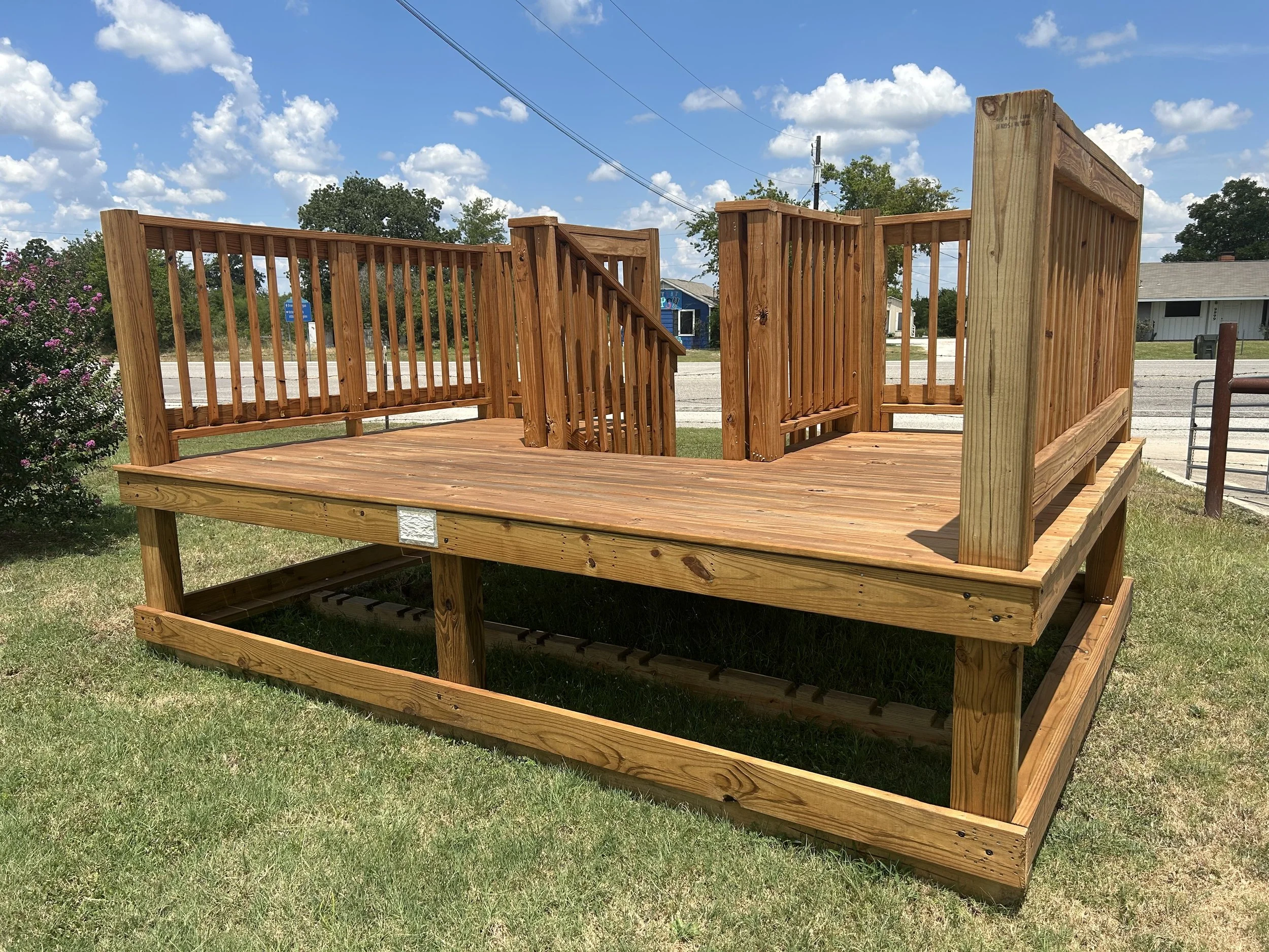 unfinished wooden deck with railings and stairs outside on a grassy lawn under a partly cloudy sky.