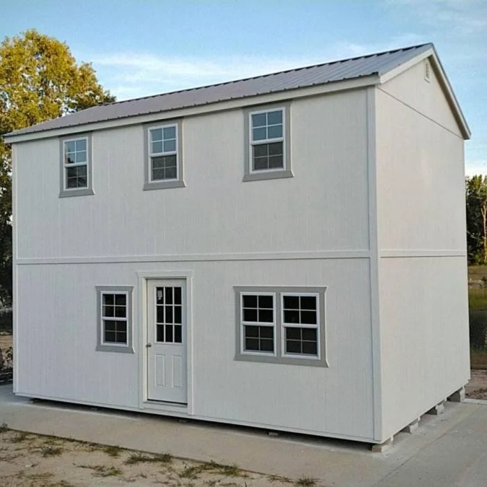 A two-story white modular building with four windows on each floor, a door on the ground floor, and a metal roof, situated outdoors on a concrete foundation.