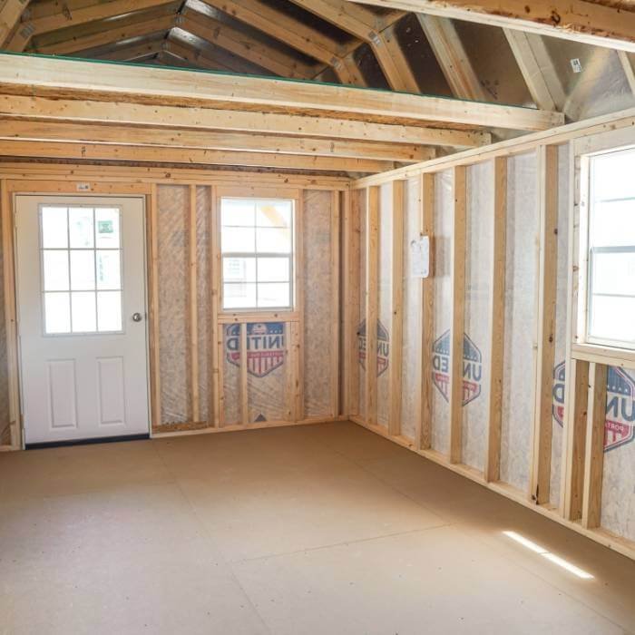 Interior of a room with exposed wooden framing, windows, door, and unfinished walls.