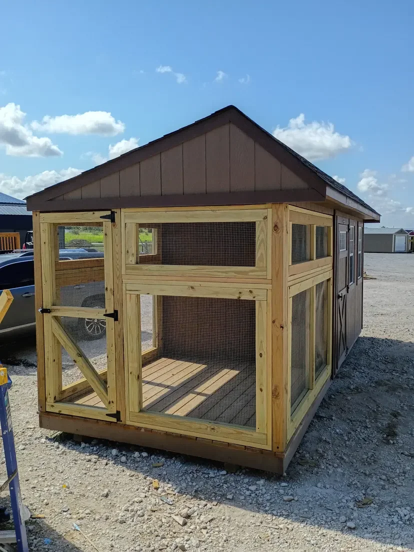 A newly built wooden chicken coop with wire mesh doors and windows, set outdoors on a gravel surface under a partly cloudy sky.