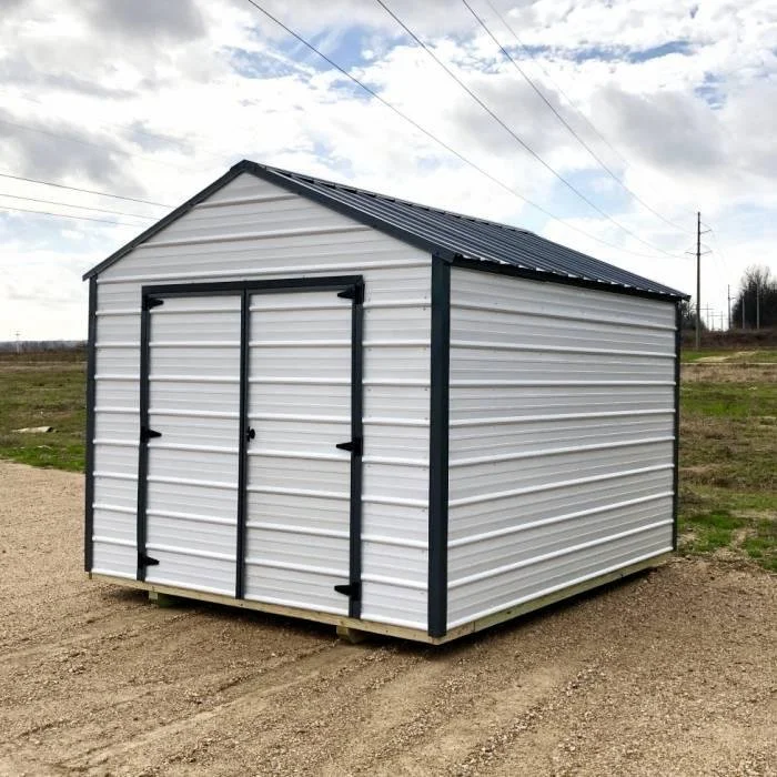 A small metal storage shed with double doors, situated outdoors on a dirt area with a grassy field.