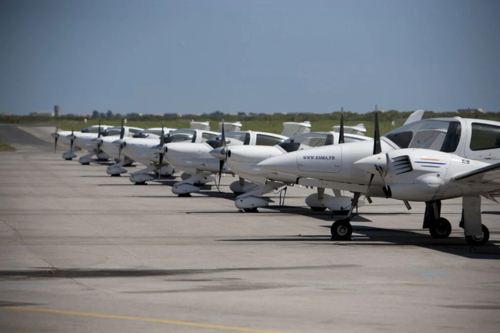 A row of white small private airplanes parked on an airport tarmac under a clear sky.