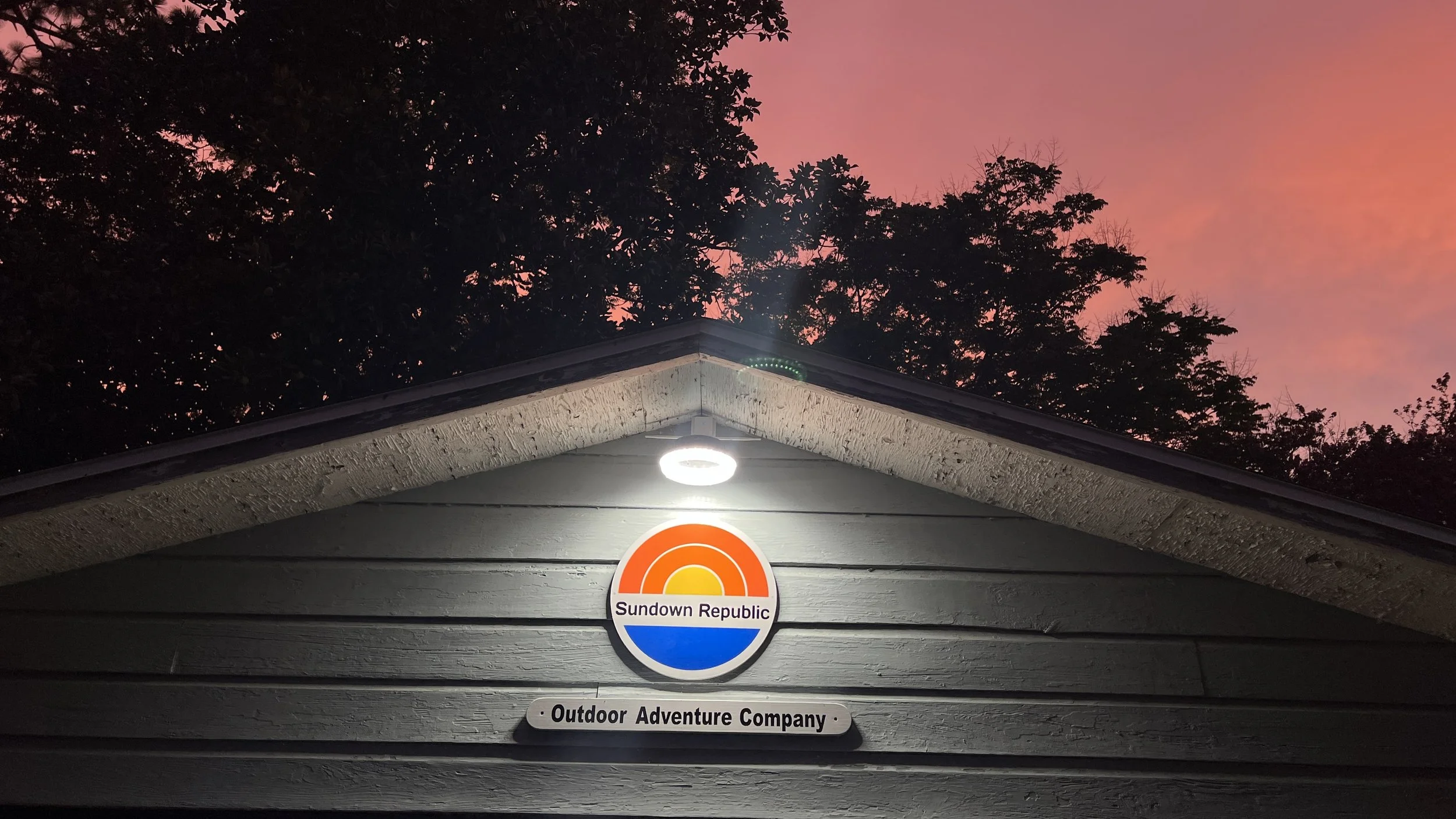 Sign reading Sundown Republic Outdoor Adventure Company with pink and orange sunset sky