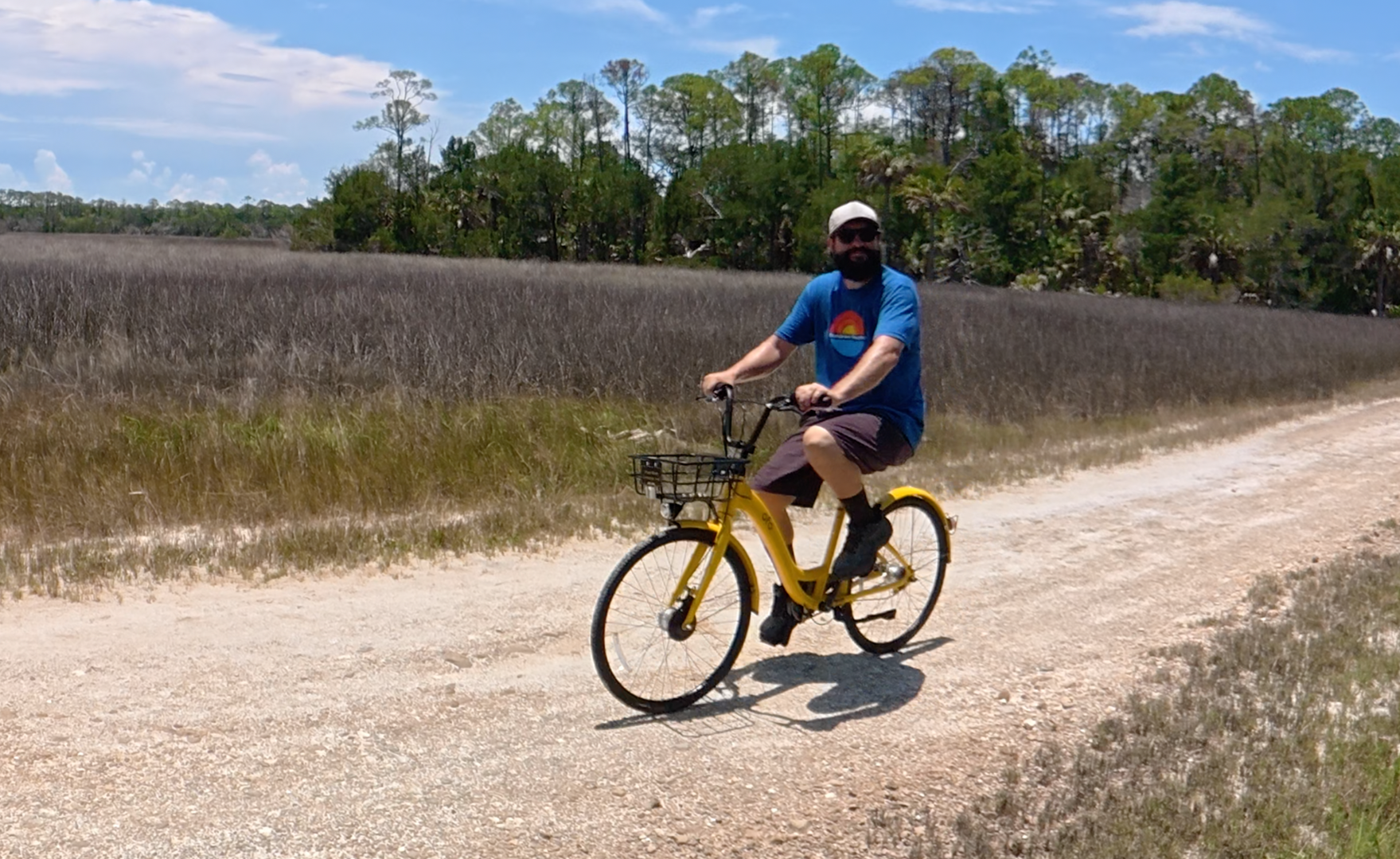 Man riding a yellow bike along an unpaved path through the marsh