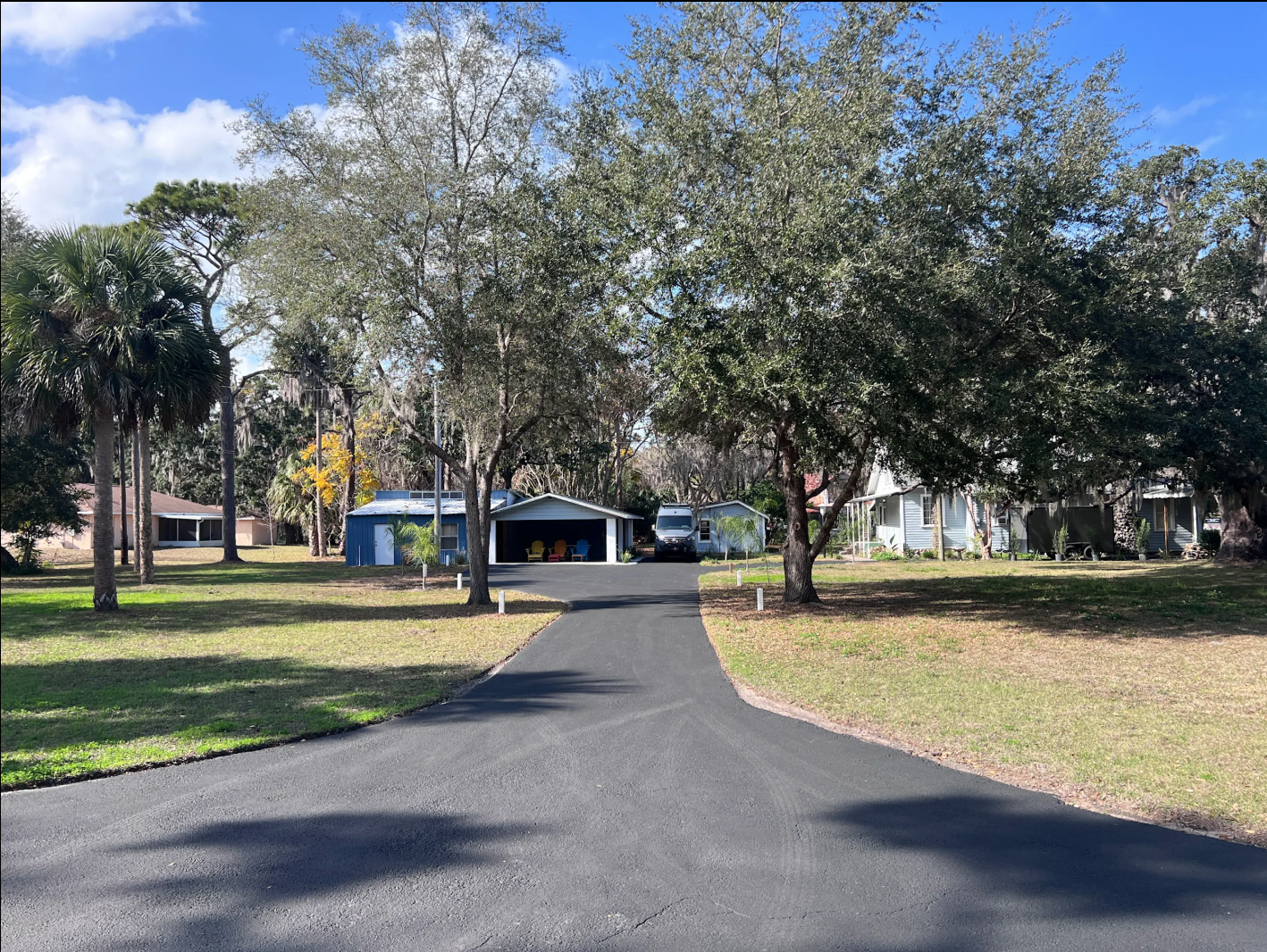 Main entrance to Sundown Republic. Asphalt driveway with grass, oak trees and palm trees leading to parking area
