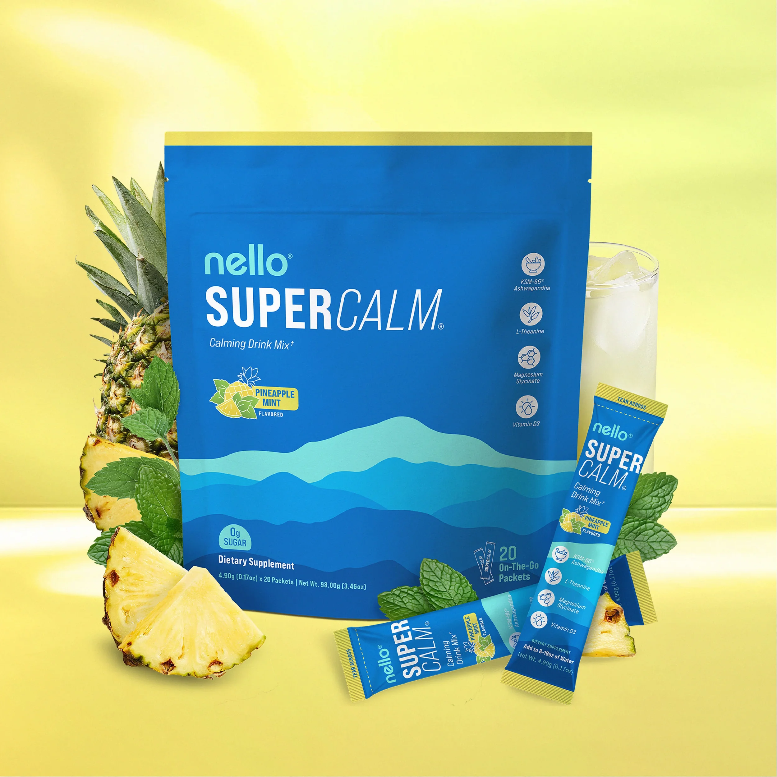 The image shows a blue package of Nello Super Calm calming drink mix with pineapple mint flavor, along with fresh pineapple slices and mint leaves, all set against a yellow background. There are also two smaller packets of the drink mix and a glass f