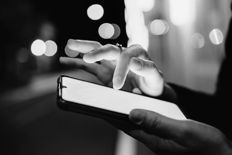 A person using a smartphone at night with bokeh city lights in the background.