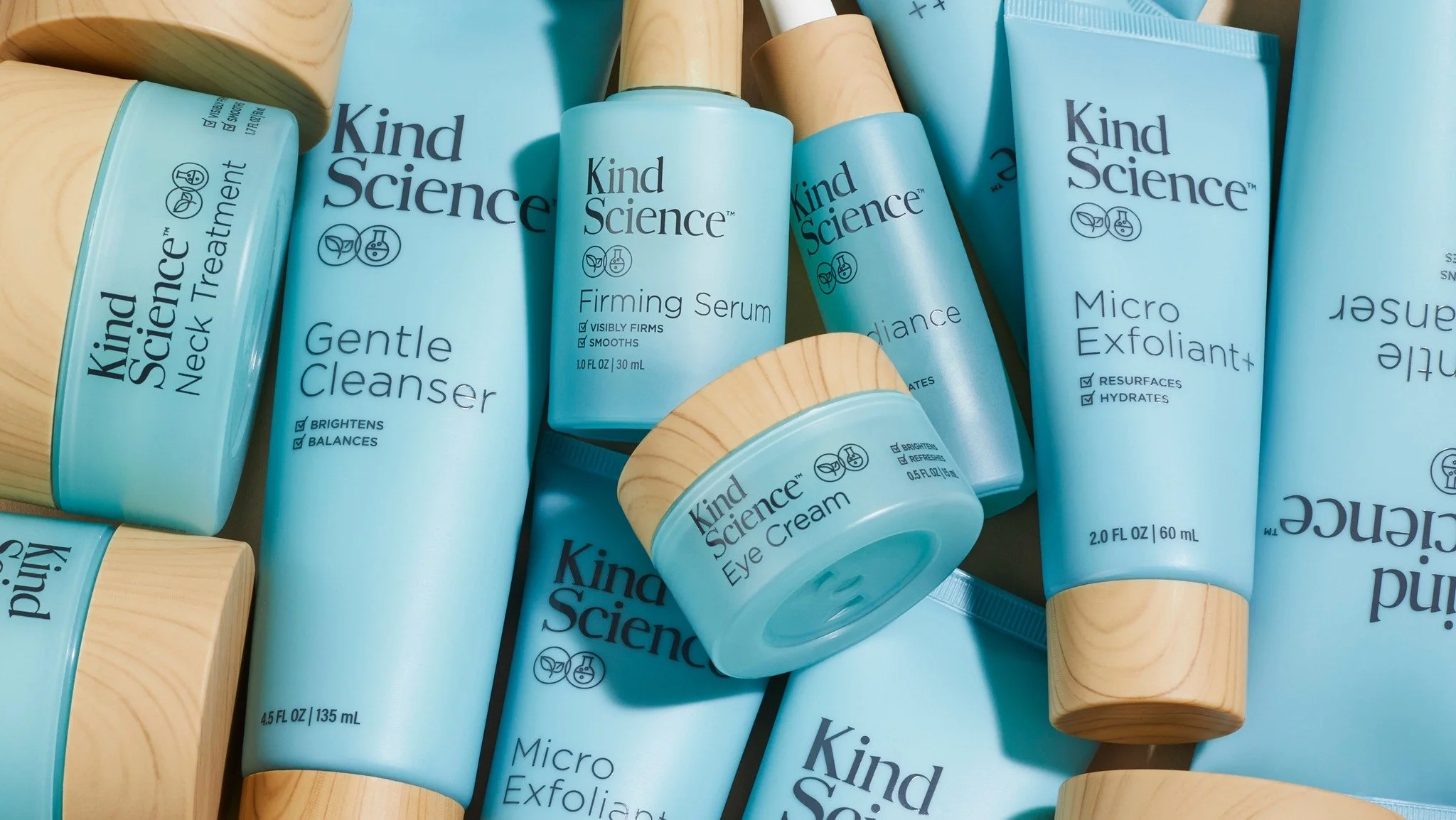 Collection of light blue skincare products from the brand Kind Science, including Gentle Cleanser, Firming Serum, Eye Cream, and Micro Exfoliant, with wooden accents on the packaging.