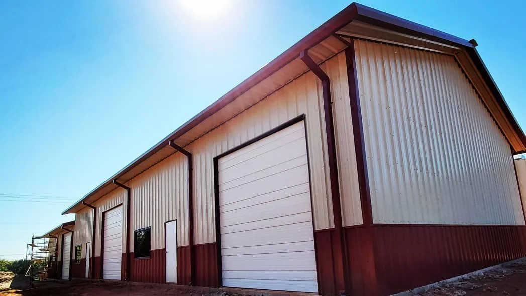 Cream colored metal building with brick red wainscoting and gutters, and white garage doors