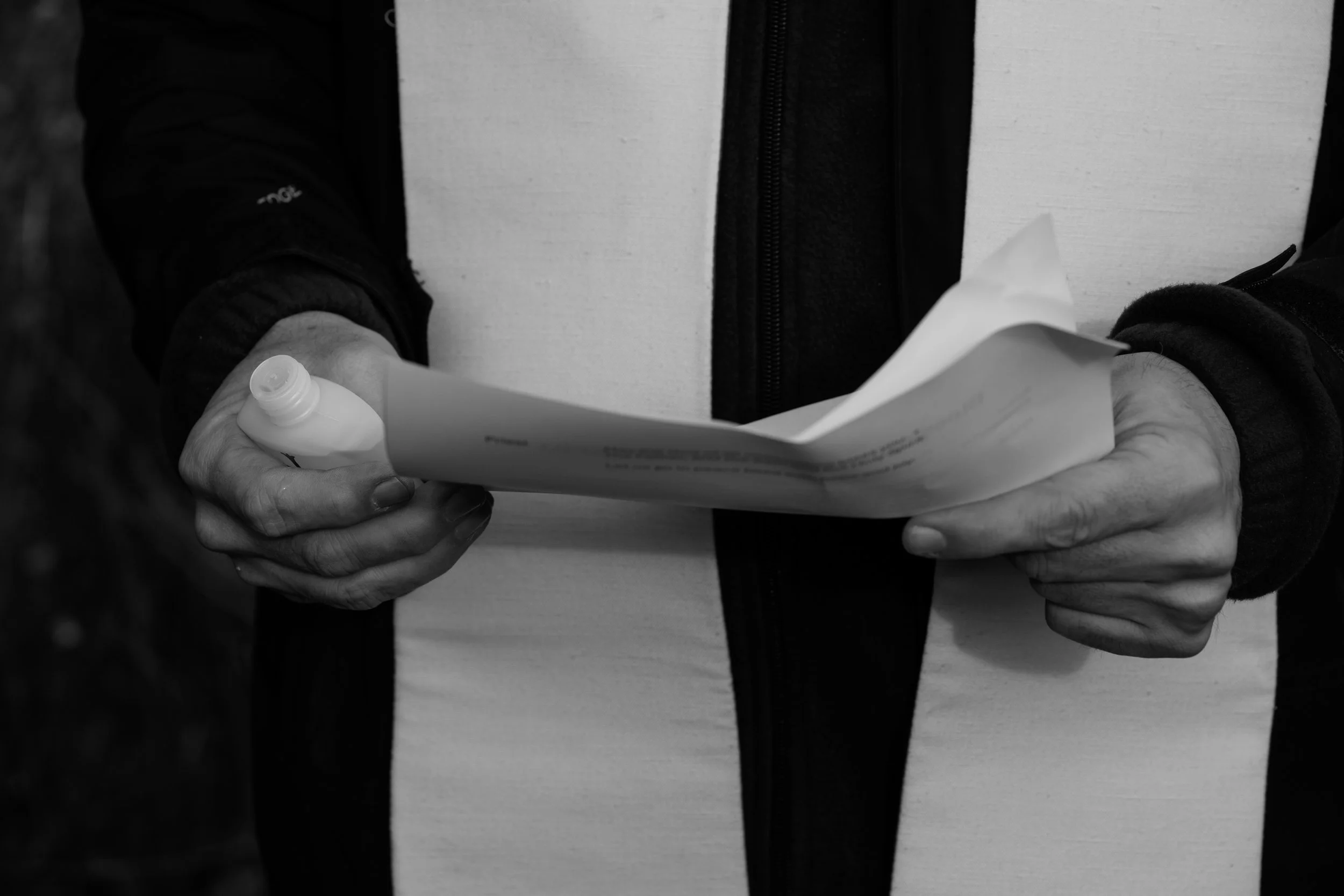 A person holding a piece of paper and a pen, dressed in a white jacket and black outerwear.