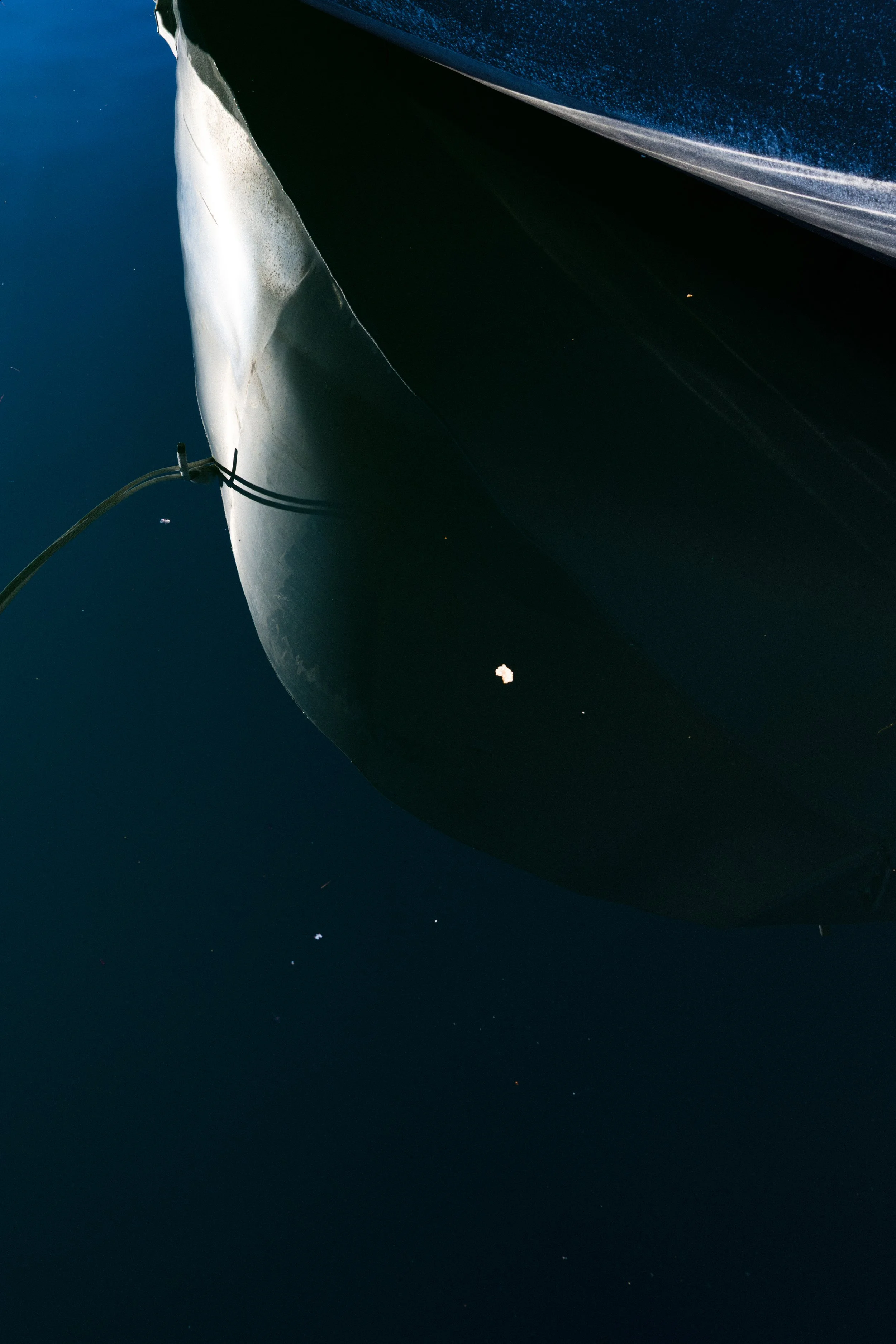 Close-up of a boat's hull reflecting in dark water, with a rope tied to the bow.