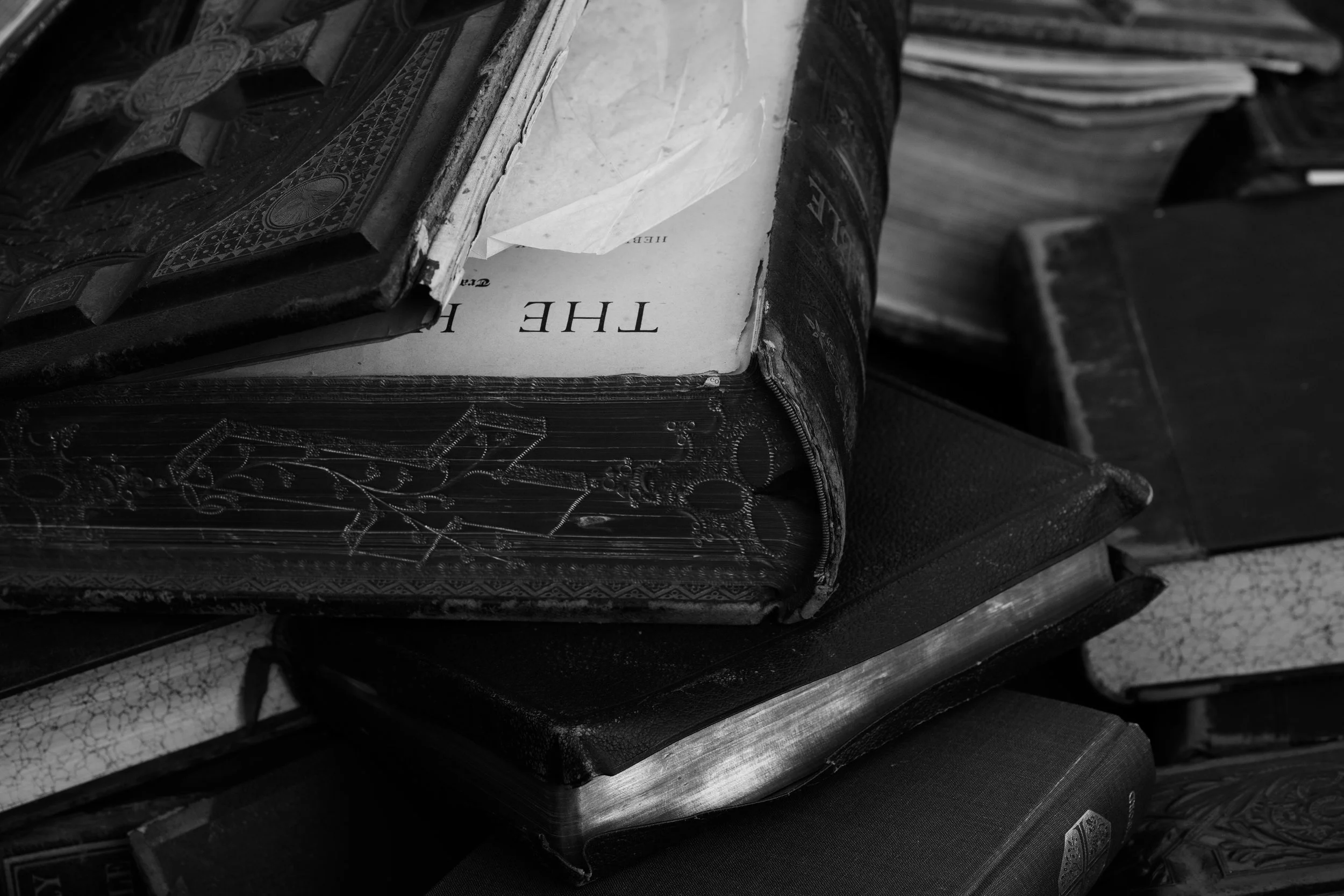 Stack of old, worn books with a partially opened book on top, showing a page titled 'THE' in black and white.
