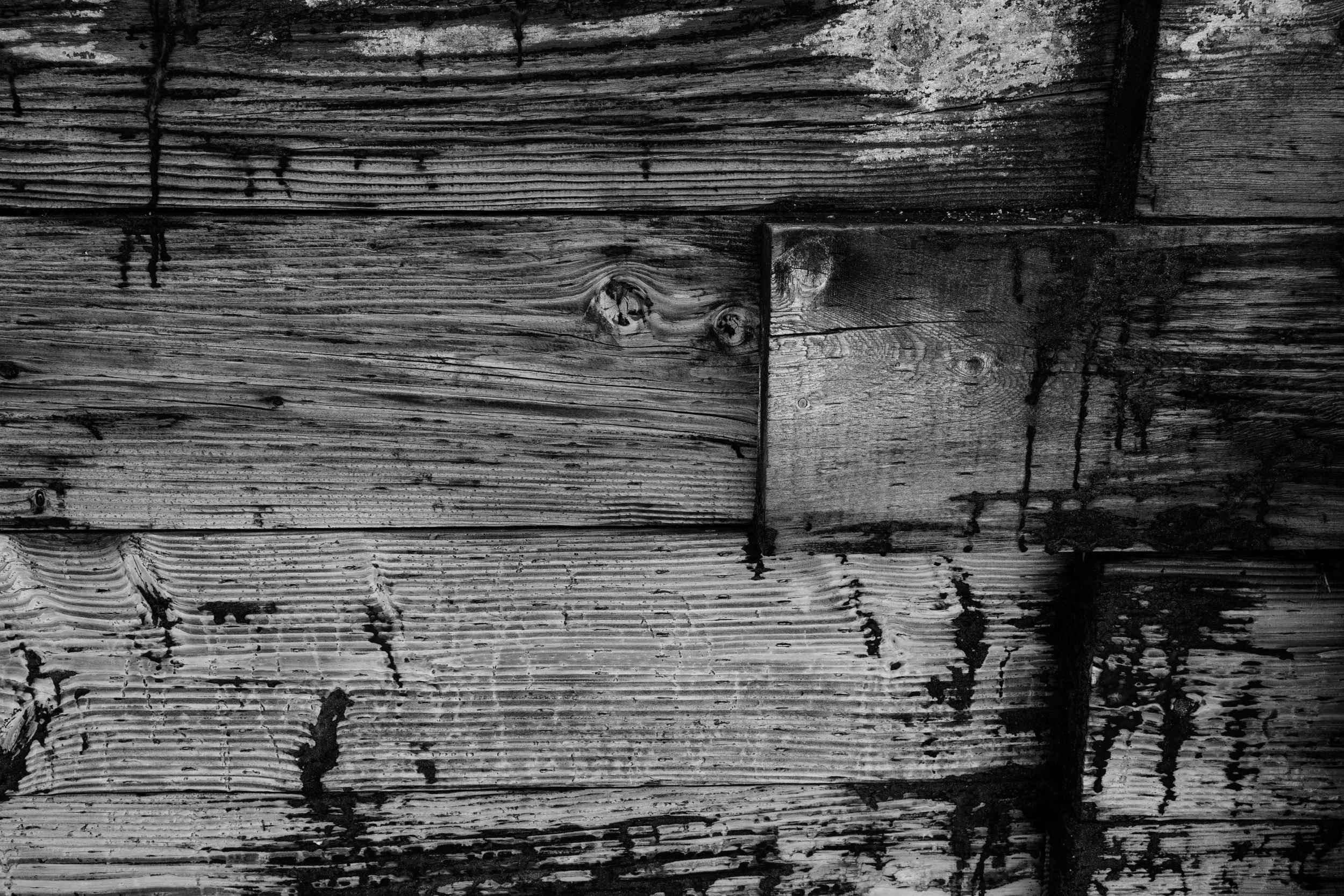 Close-up of weathered wooden planks showing knots, grain, and dark stains in black and white.