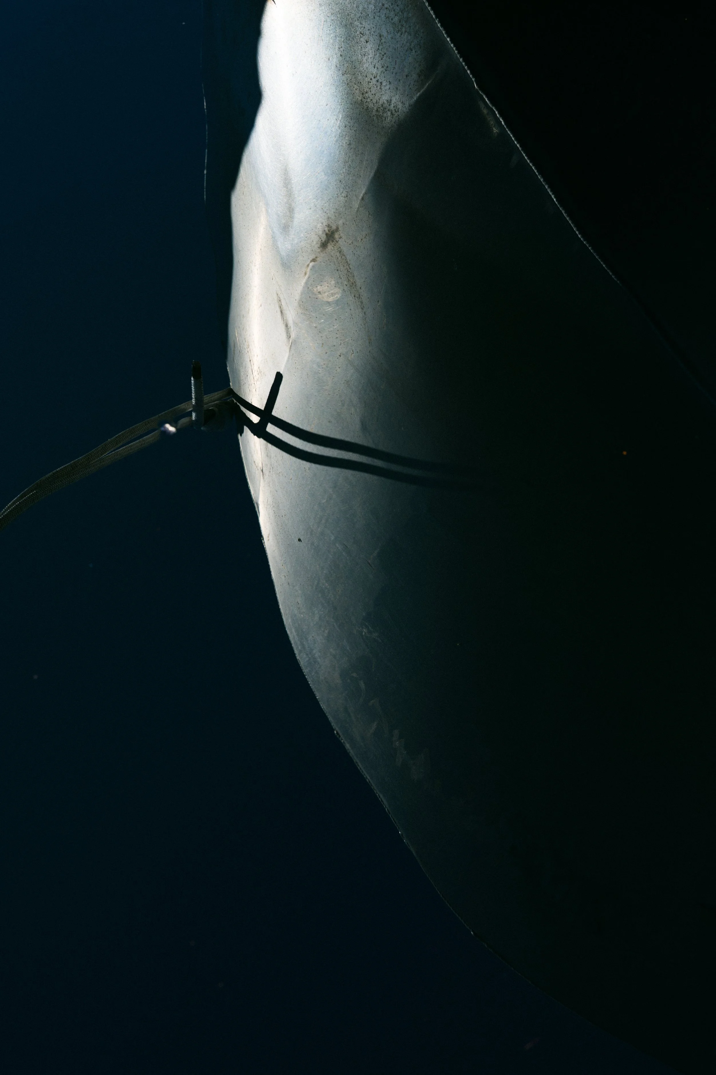 Close-up of a metallic surface, possibly part of a spacecraft or submersible, with a dark background and a cord or cable attached.