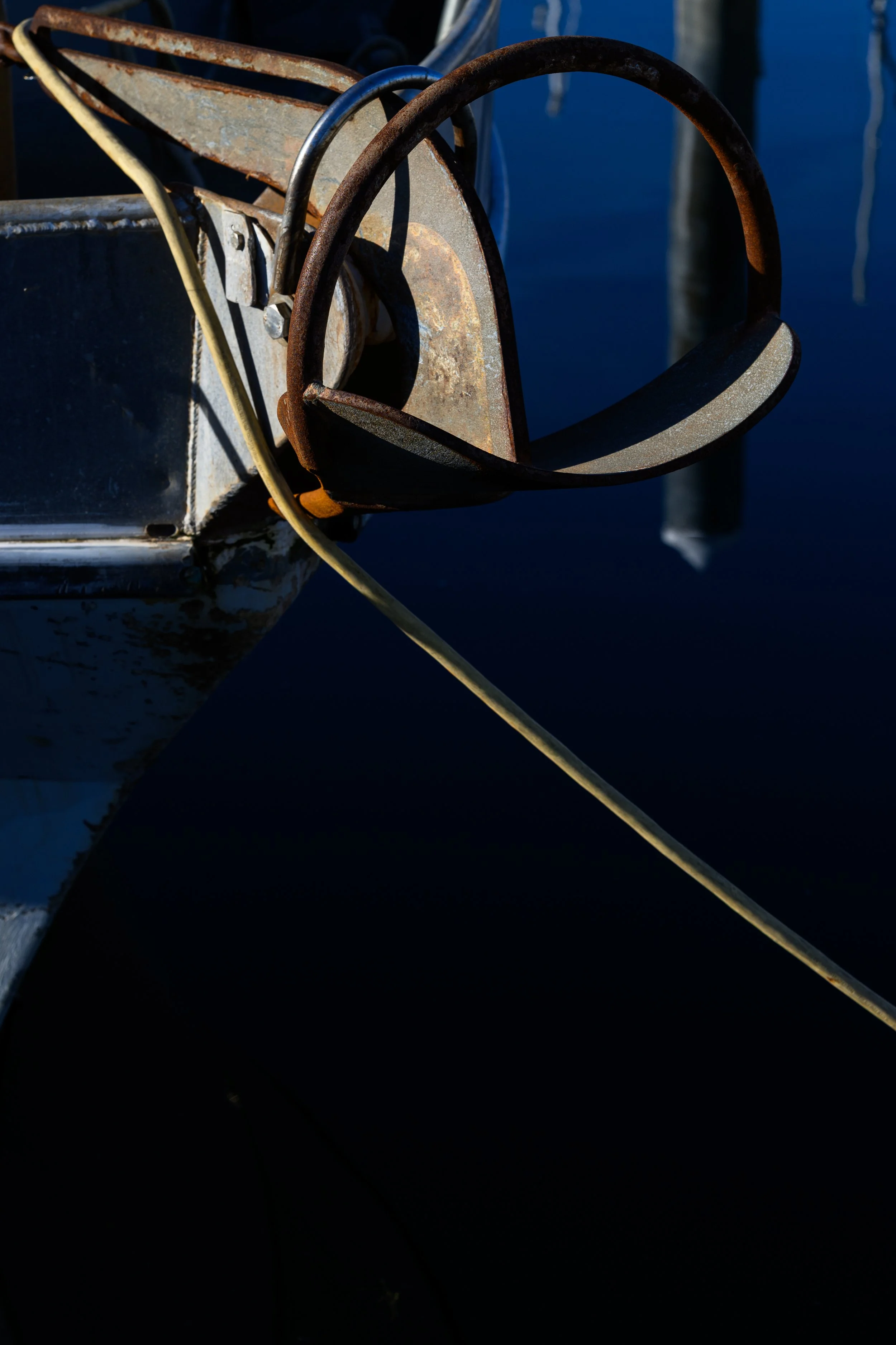 Close-up of an old, rusted boat anchor attached to the bow of a boat with a fishing line extending into the dark water.