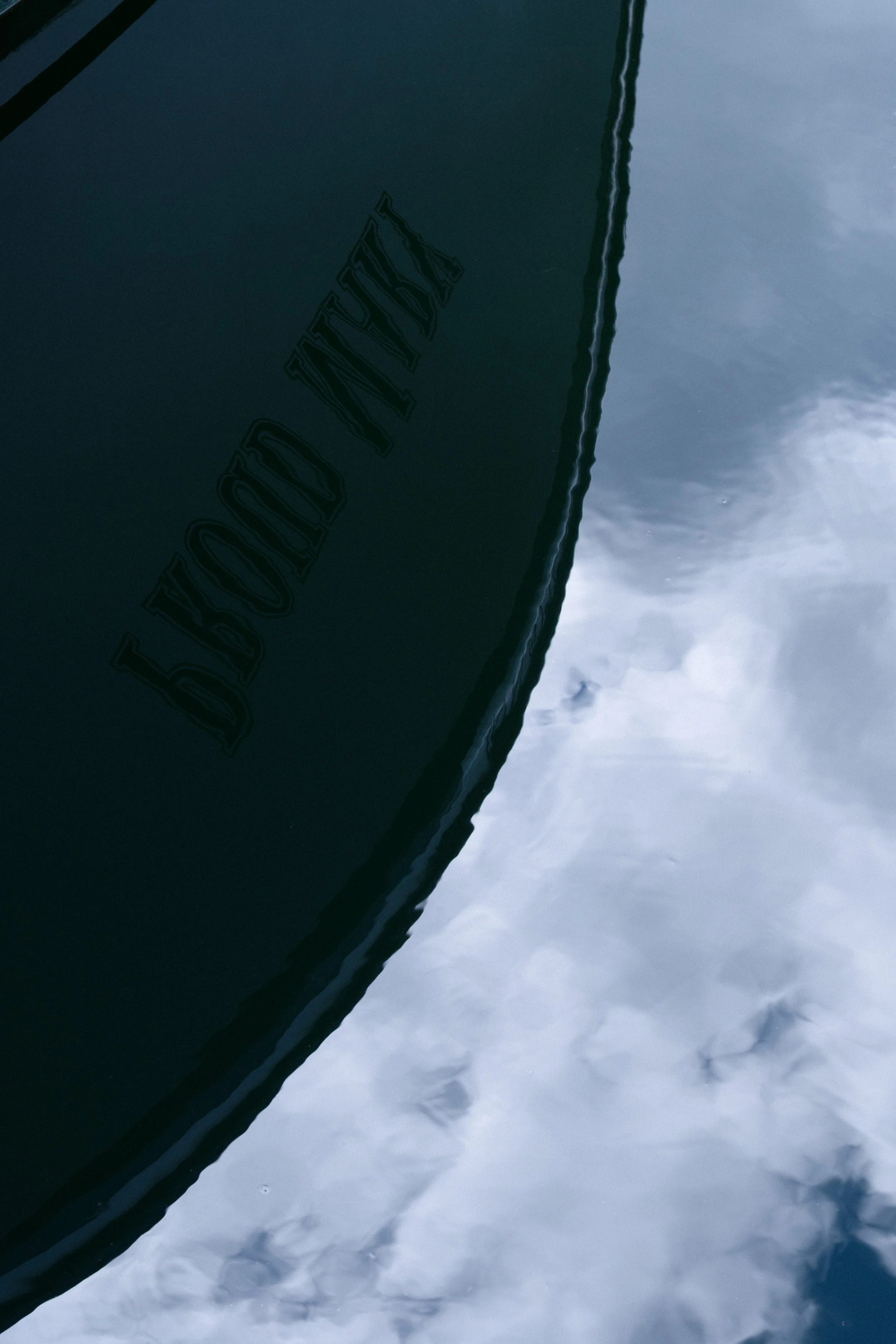 Close-up of a boat with the brand name 'LADY LIBERTY' on the side, floating on water with clouds reflected on the surface.