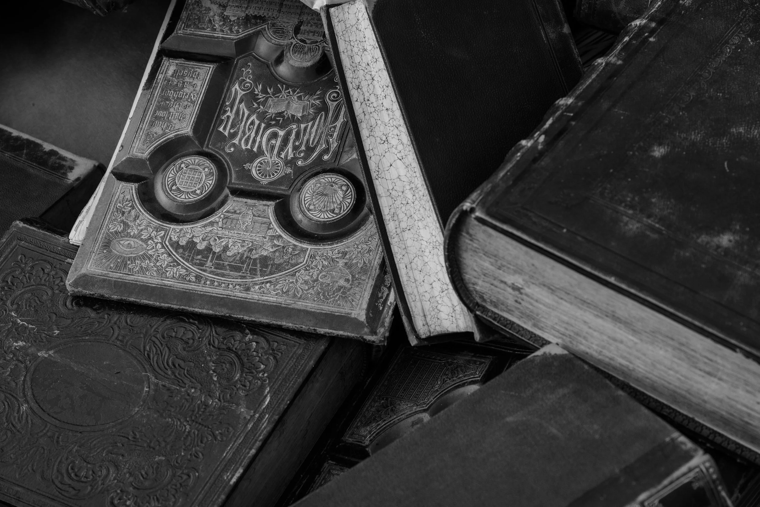 Close-up of old, worn books stacked on top of each other, with some showing ornate and detailed covers.