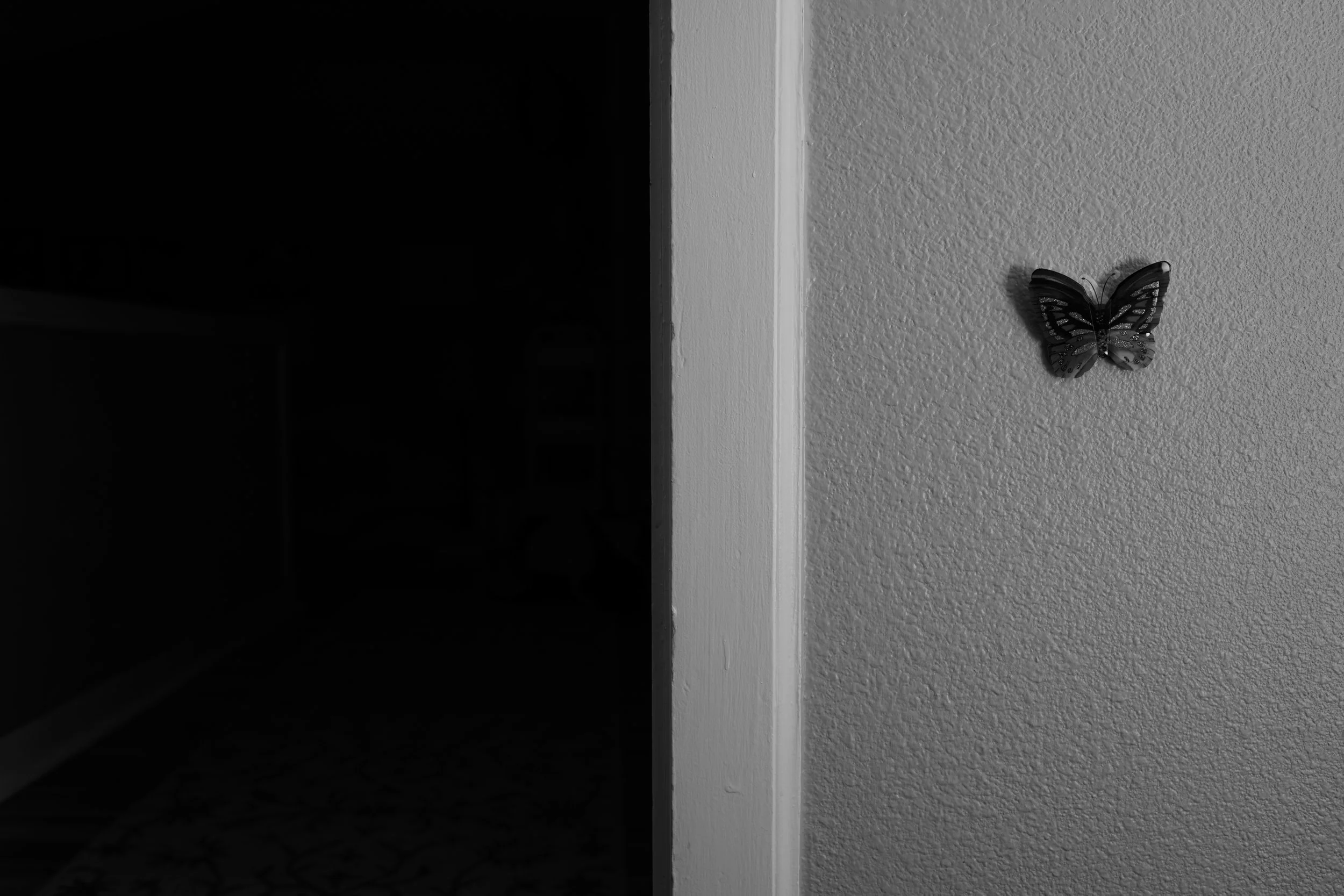 A gray textured wall with a black butterfly-shaped ornament on it, contrasted by an adjacent dark doorway.