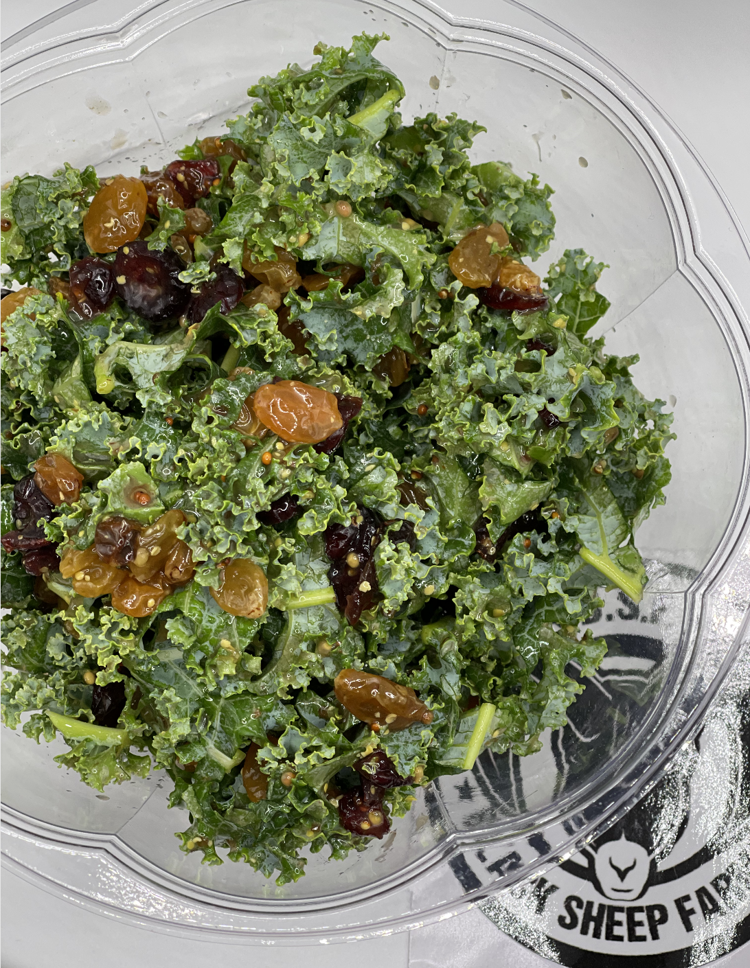 Kale salad with dried cranberries and seeds in a clear plastic container.