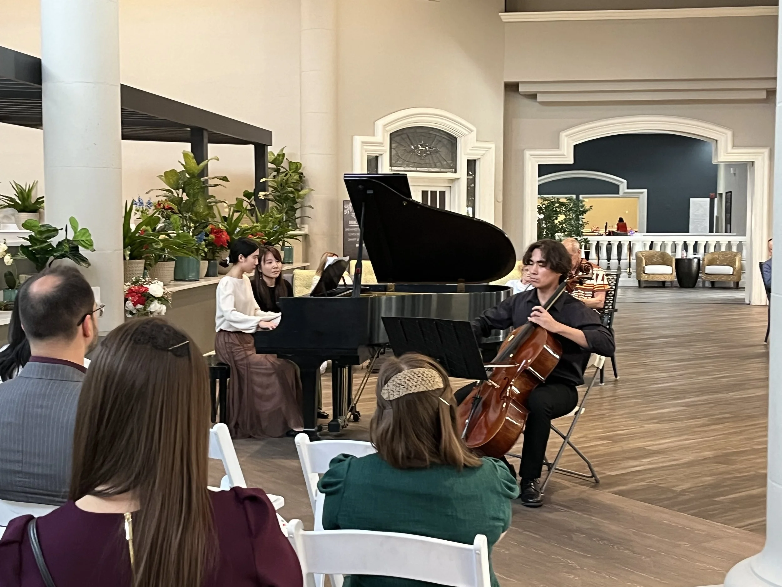 Musicians performing with a pianist, cellist, and singer at a live event in a decorated hall with audience watching.