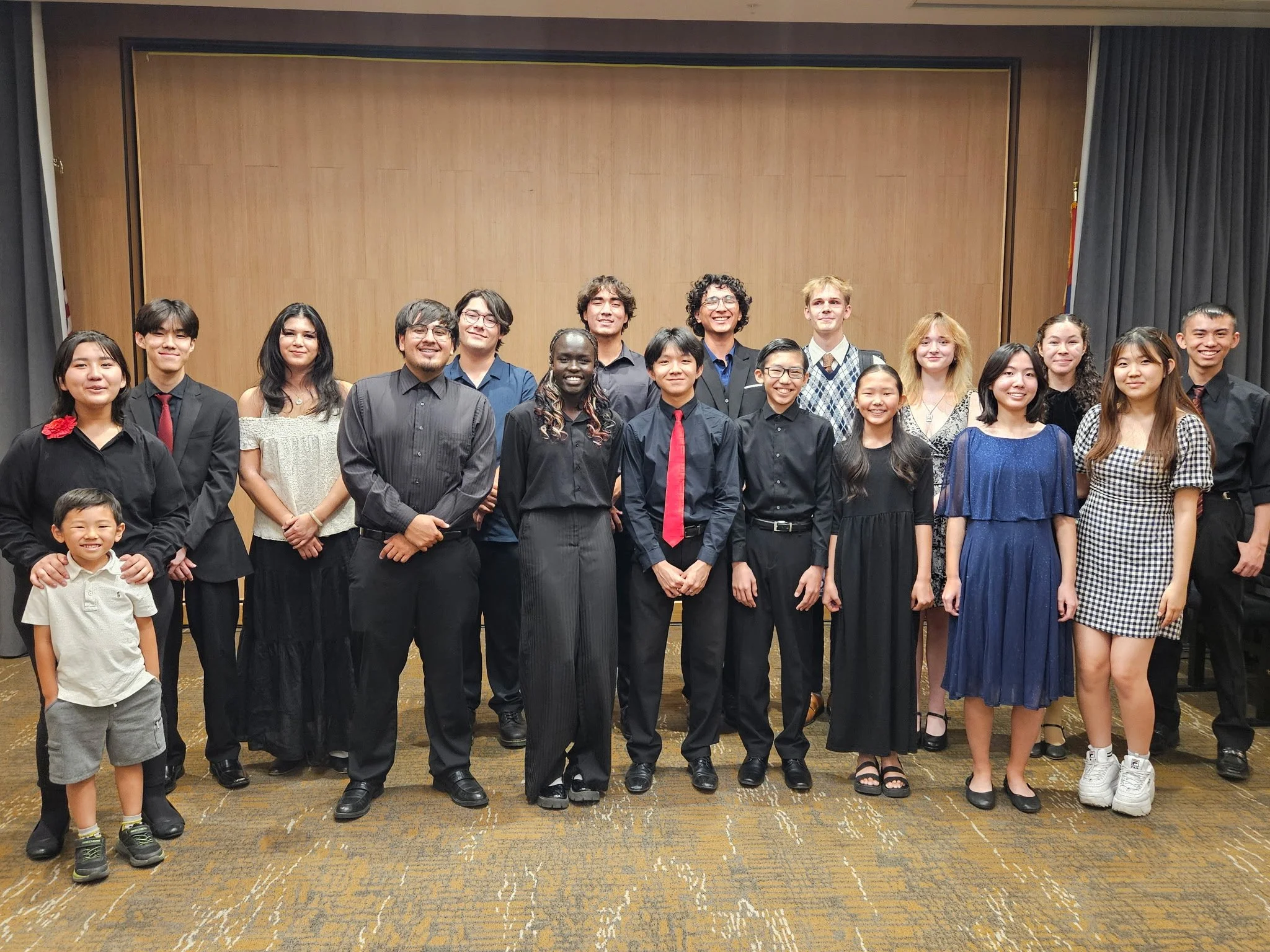 Group of young adults and children in formal attire posing together indoors in front of a wooden wall.