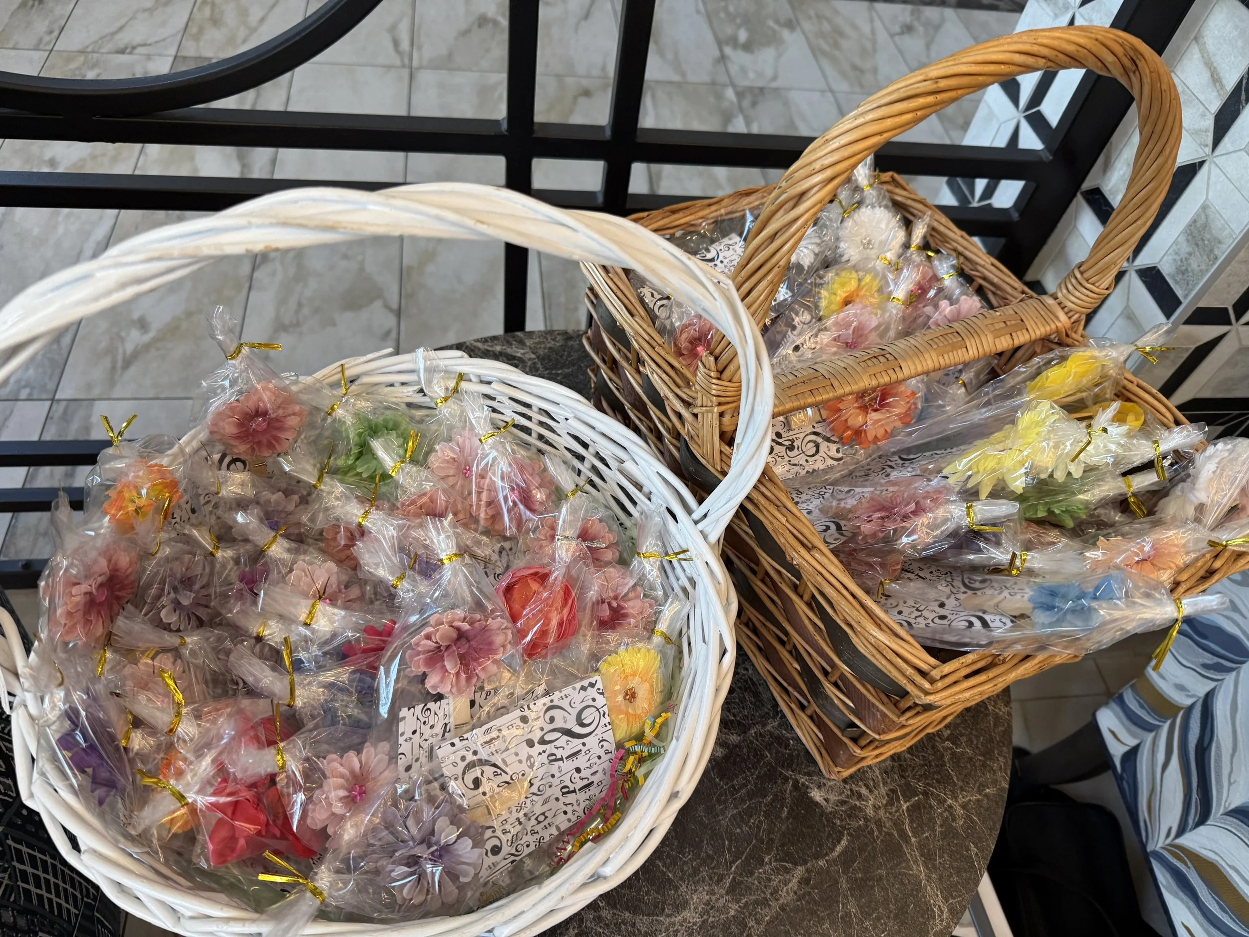 Two wicker baskets filled with individually wrapped decorative flowers, one white and one brown, on a marble tabletop.