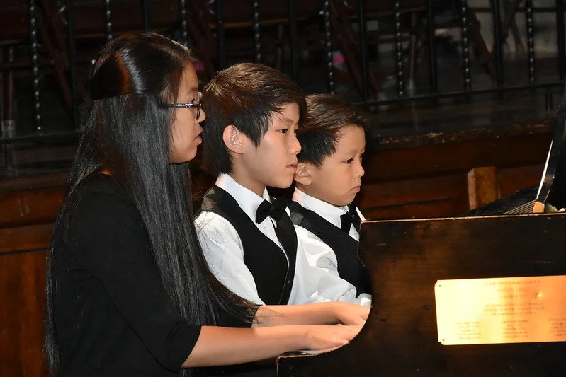 Three children dressed in formal attire playing the piano.