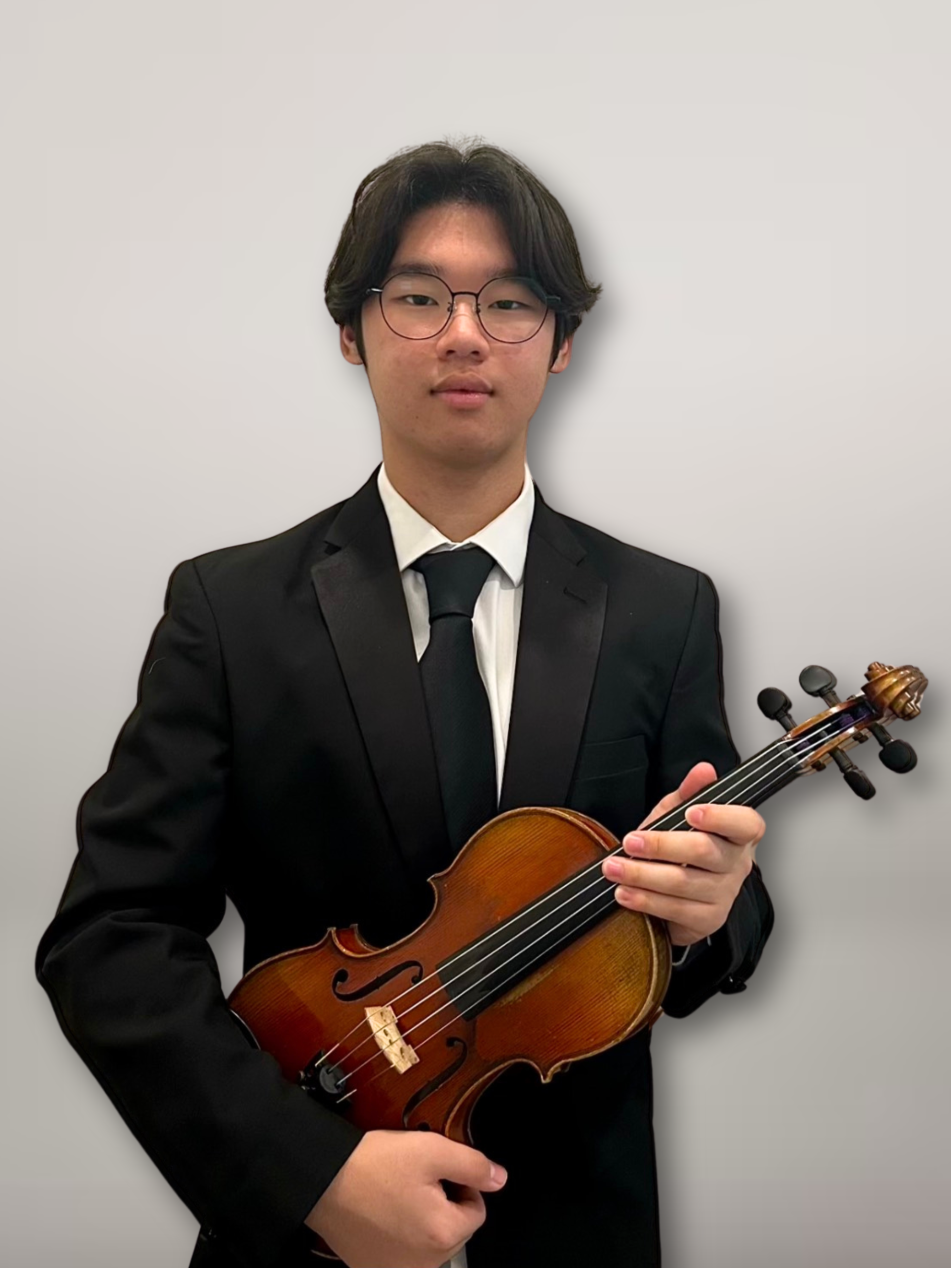 Young man wearing glasses in a black tuxedo holding a violin against a plain white background.