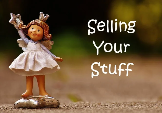 Decorative figurine of a smiling girl with wings and a crown, standing on a small silver platform, next to the text 'Selling Your Stuff' on a blurred outdoor background.