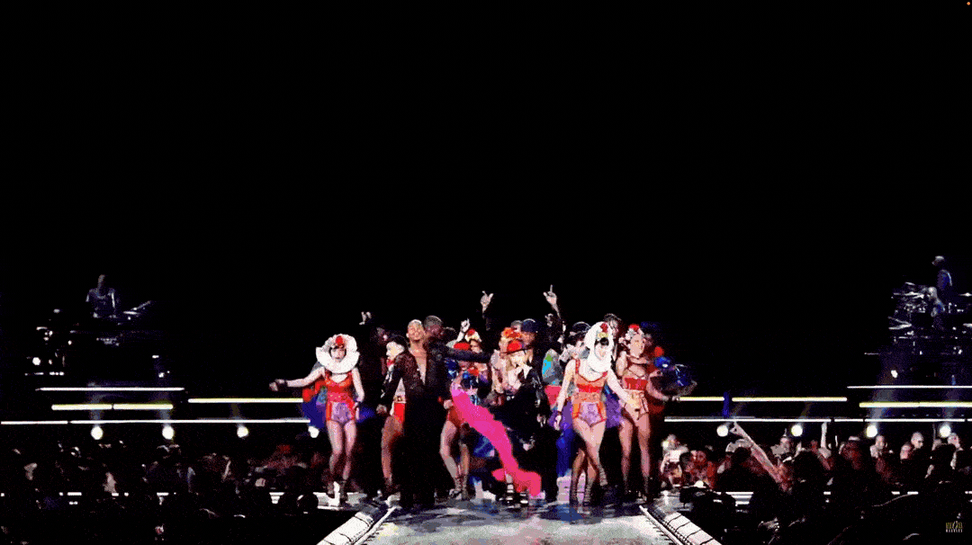 A stage performance featuring dancers in colorful costumes, with some in clown-like outfits, under bright stage lighting.