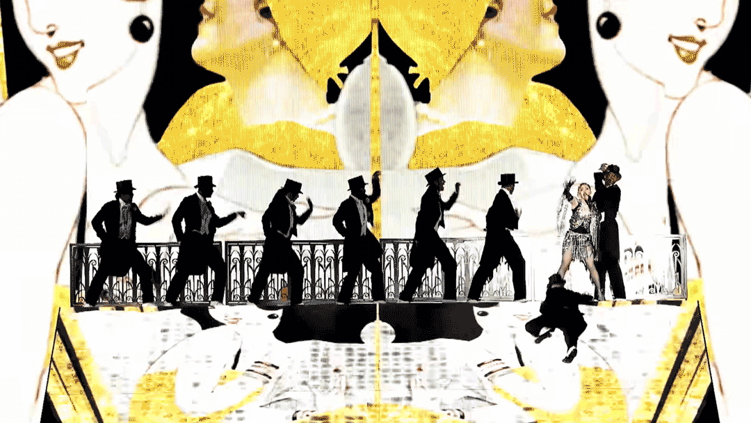 A theatrical stage scene with performers in black suits and hats, two women in glittering costumes, and a large colorful backdrop of stylized smiling women.