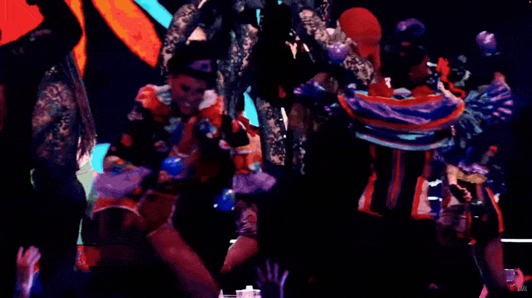 A group of people in historical costumes performing a traditional dance in a dark setting with colorful lighting.