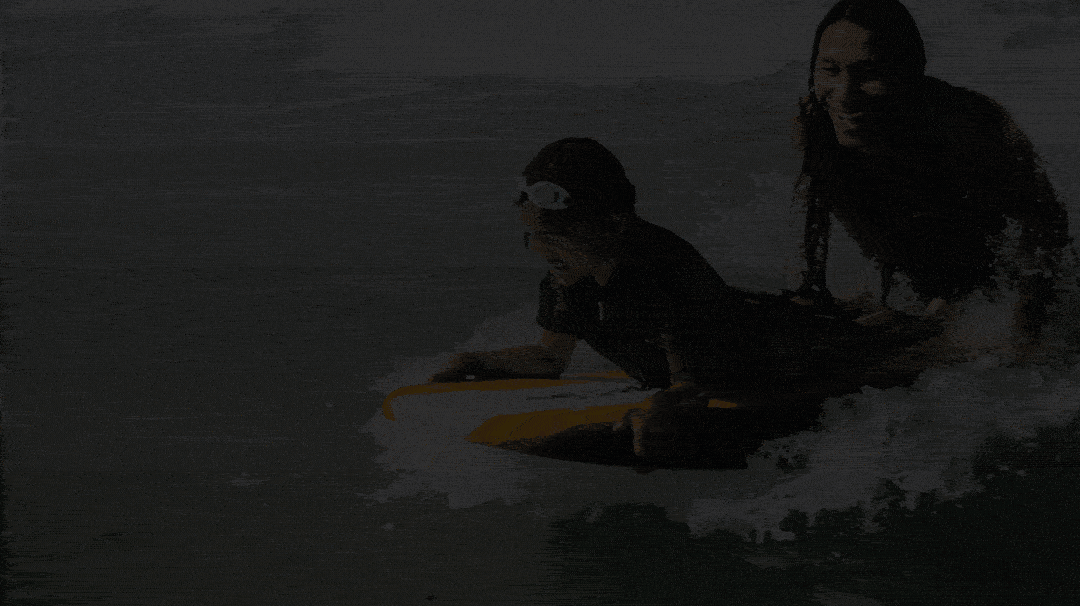 A woman and a child riding a yellow surfboard in the water.
