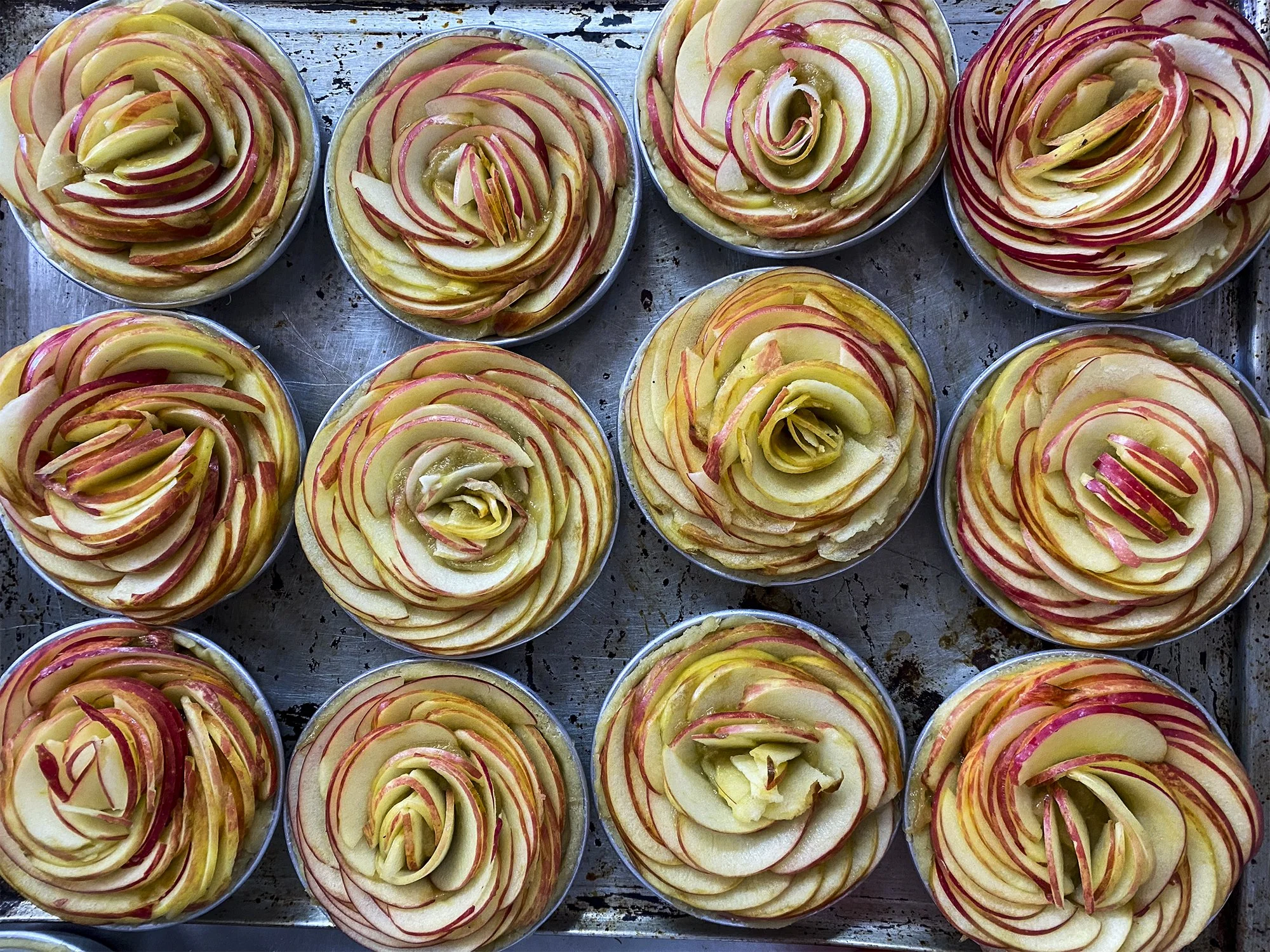 Postres en forma de rosas hechas con manzanas en moldes metálicos.