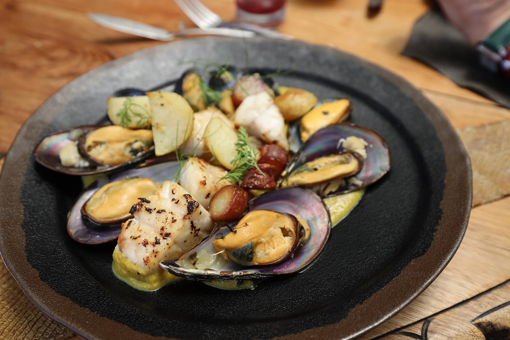 Mejillones con papas, hierbas y salsa en plato de piedra.