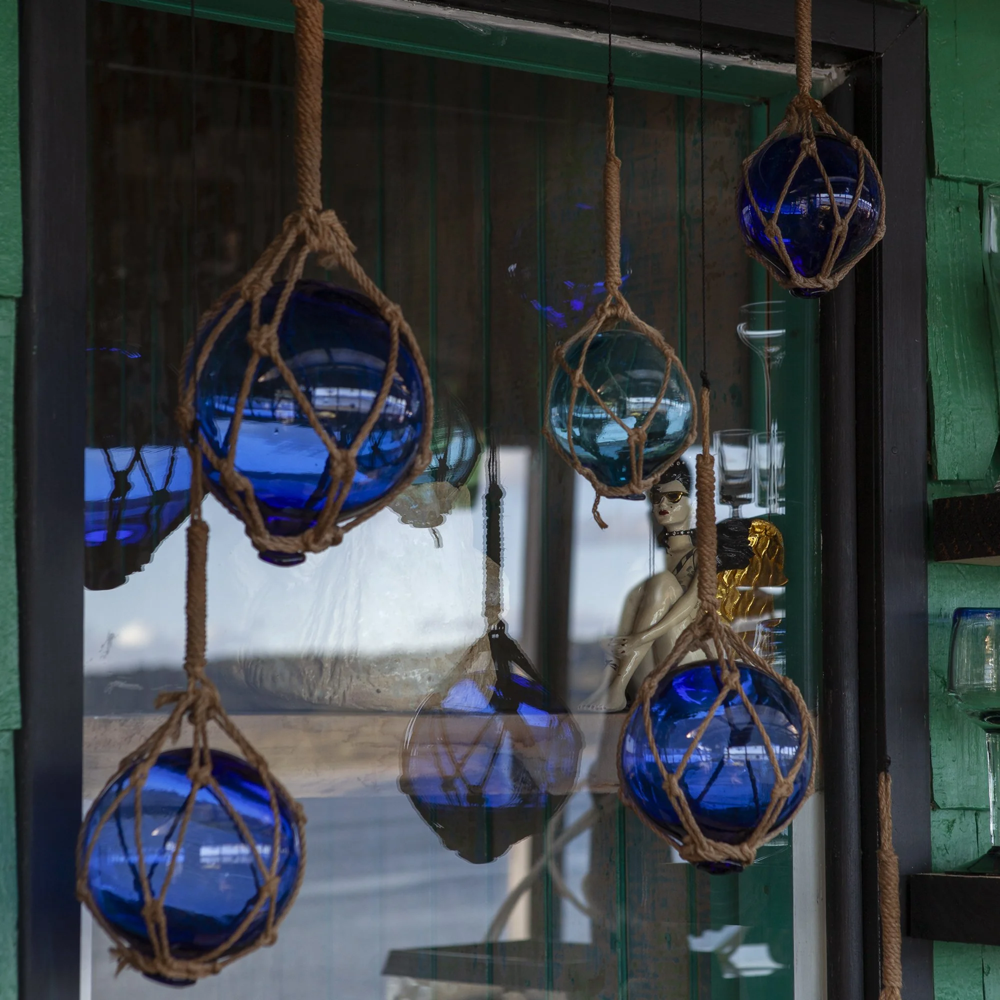 Vasos de vidrio azul enredados con cuerda, colocados en una vitrina con figura de una mujer y objetos decorativos.